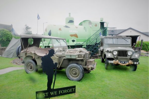 A rainy photo of some vehicles and Sir James outside The Devil's Porridge Museum.