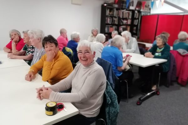 Three rows of tables with members of The Devil's Porridge Museum's Cordite Club sat at them. The person closet to the camera looks very happy.