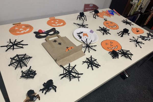 A table containing items that the young people at this workshop has made. This includes paper pumpkins, a few masks, one trick or treat bag, pipe cleaner spiders and spiders webs.