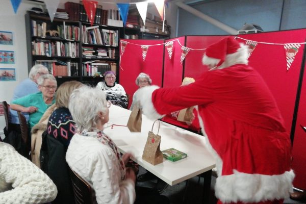 Santa gives out Christmas gift bags to a table of people.