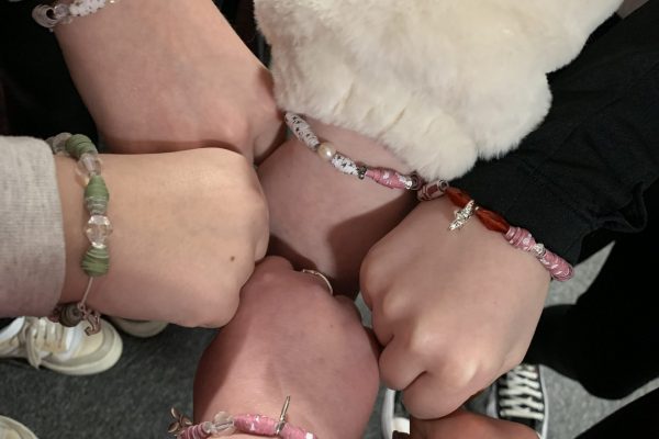 A circle of hands wearing bracelets.