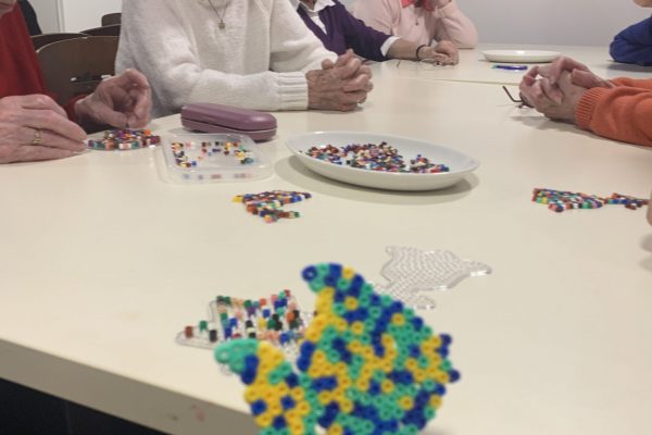 A fish shape made out of Hama beads with some members of the museum's Cordite Club in the background.
