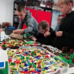 Lego bricks with some people building Lego designs in the background.